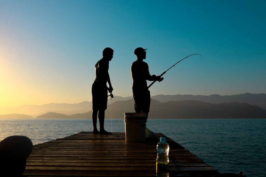 夕暮れの波止場で釣り竿を持つ人のシルエット