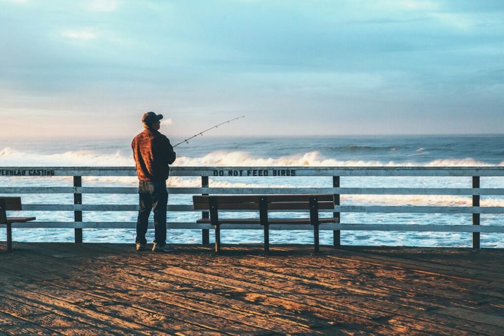 日の出の杉で釣り竿を持ち釣りをする人のシルエット