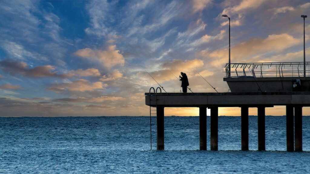 夕焼け空の下、海に突き出た桟橋で釣りをする人