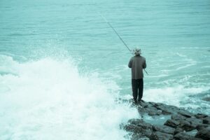 波が打ち寄せる岩場から海へ竿を向ける釣り人