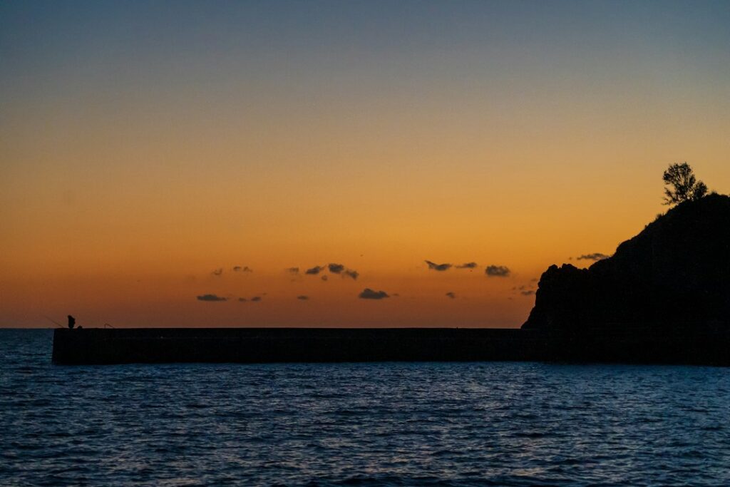 夕暮れ時、海に突き出た桅橋で釣りをする人のシルエット
